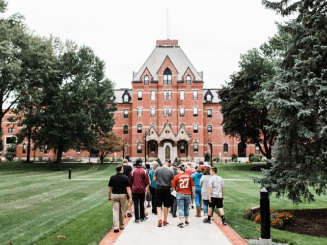 A group of students walking up the lawn toward a brick college hall
